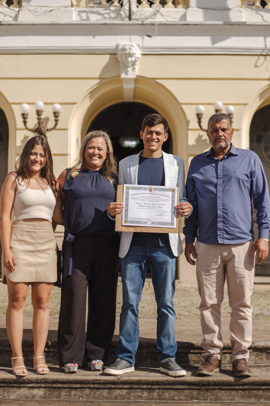 Rafael Lima com a família — Luísa, Roberta e Sérgio — segurando o diploma de vereador em frente ao prédio do Tribunal Eleitoral
